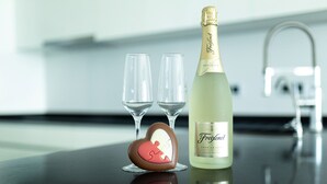 Une bouteille de champagne Freixenet, deux verres vides et un chocolat en forme de cœur, le tout posé sur une surface réfléchissante.