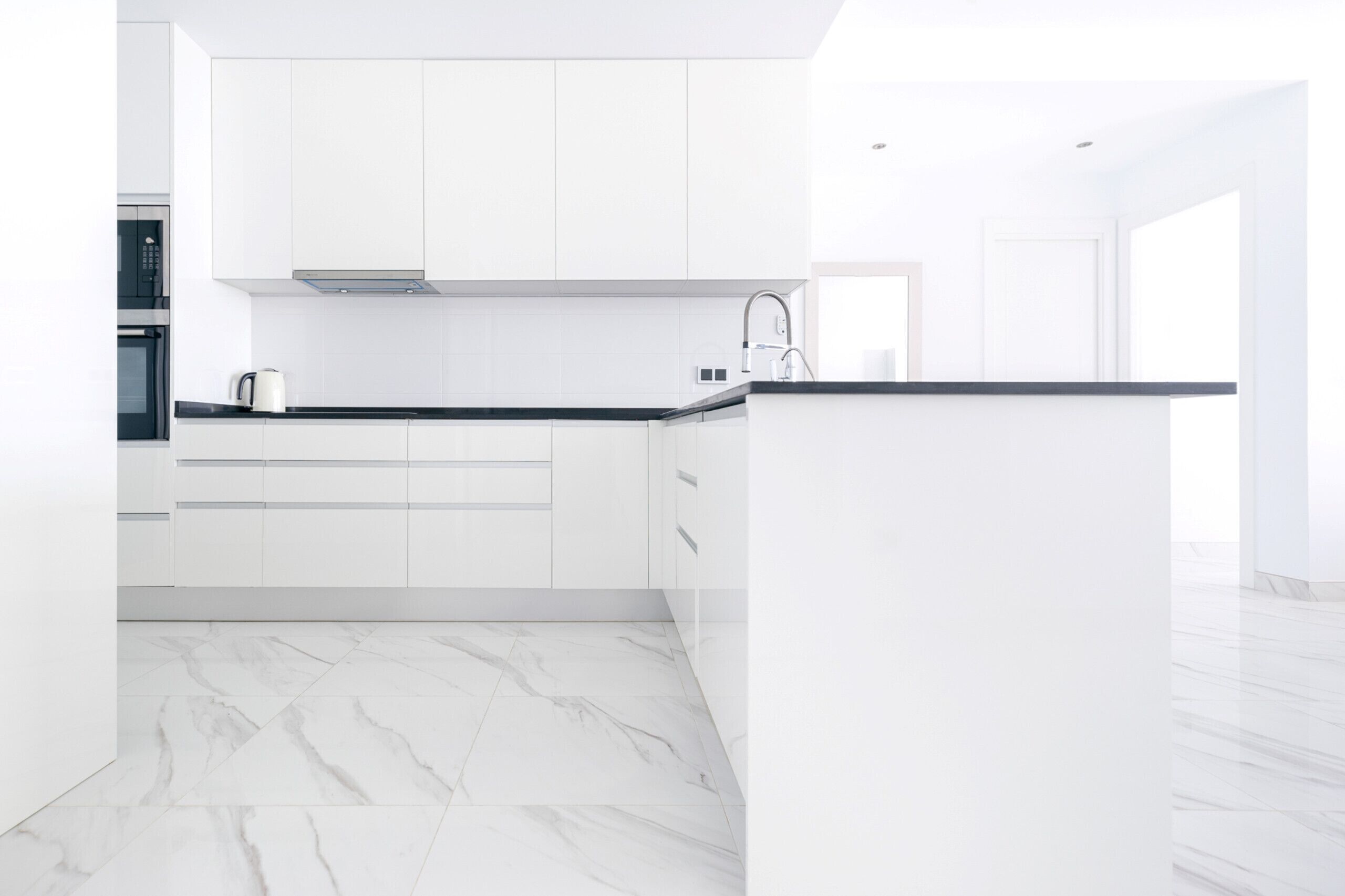 A modern kitchen with white cabinetry, a black countertop, and a marble floor.