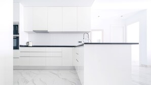 Une cuisine moderne avec des meubles blancs, un plan de travail noir et un sol en marbre.