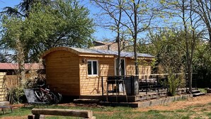 A wooden cabin with a metal roof, surrounded by trees and a grassy area. - Roulotte in the heart of the low gorges of the verdon (Quinson)