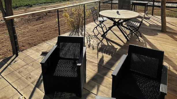 An outdoor patio with two wicker chairs and a table, surrounded by trees and a view of a green field. - Roulotte in the heart of the low gorges of the verdon (Quinson)