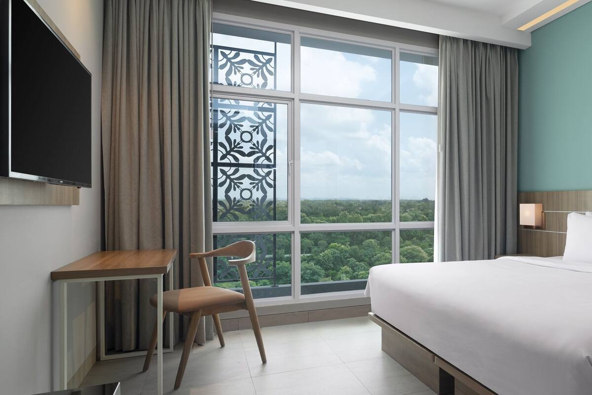 Ein Hotelzimmer mit einem großen Bett, einem Schreibtisch, einem Sessel, einem Fernseher und einem Fenster mit Blick ins Freie.