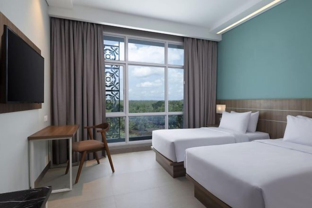 Habitación de hotel con dos camas, un escritorio, una silla y un televisor.