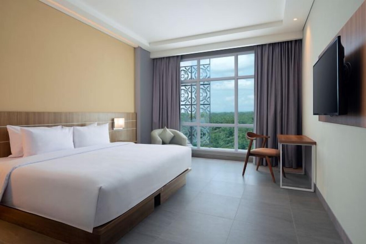 Habitación de hotel moderna con una cama grande, televisor montado en la pared y vistas a zonas verdes por la ventana.
