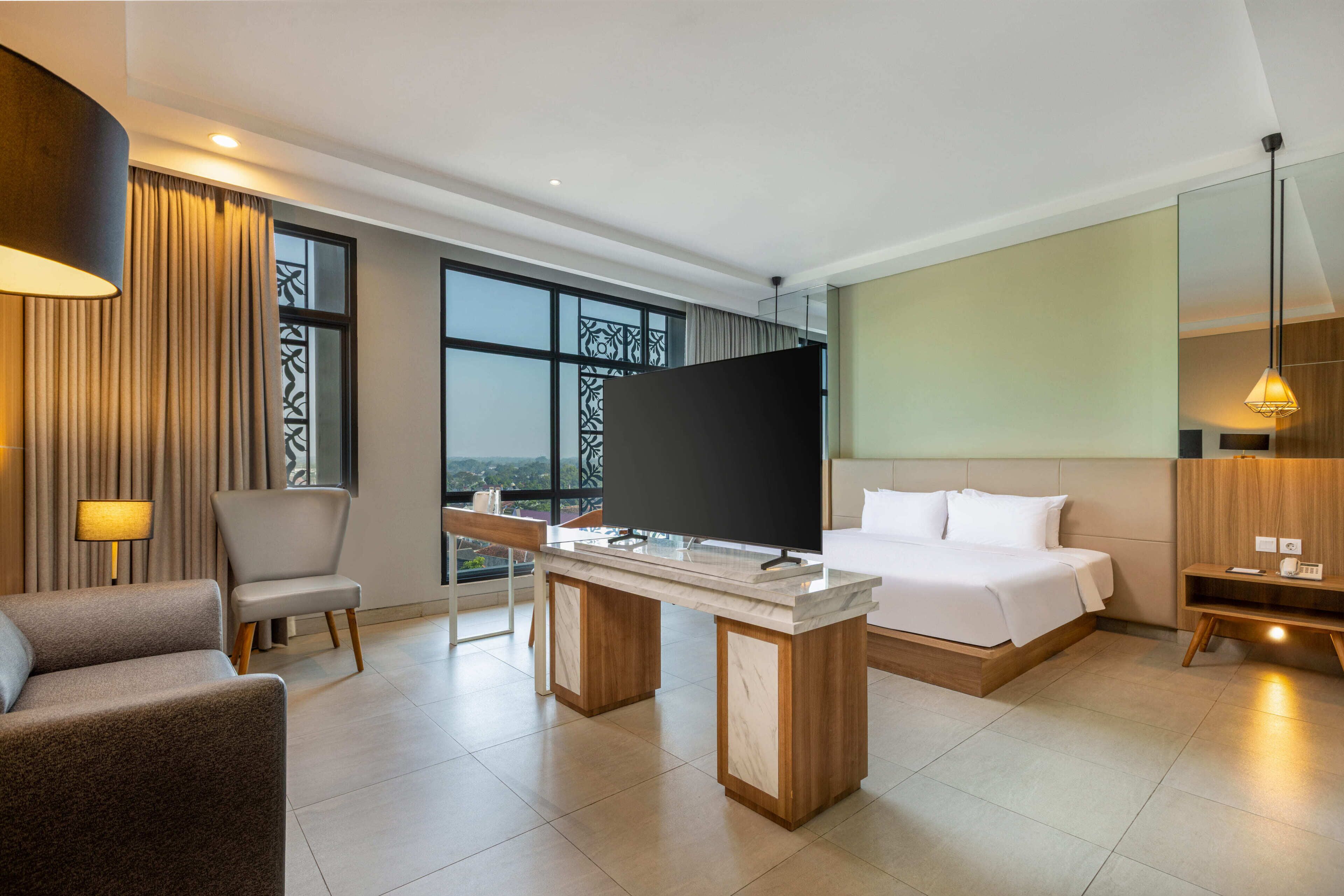 A modern hotel room with a bed, a desk, a chair, a TV, and a large window offering a view.