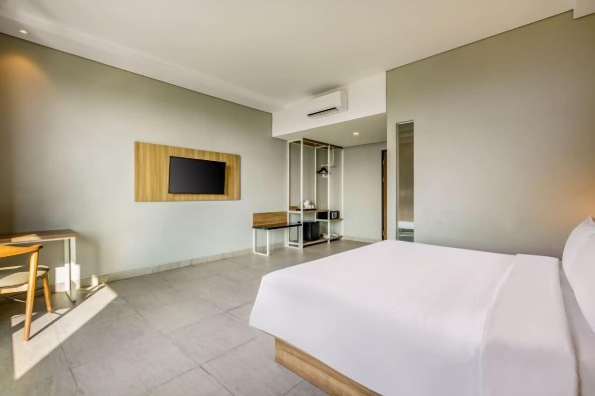 Habitación de hotel con cama, escritorio, televisor y zona de ducha.