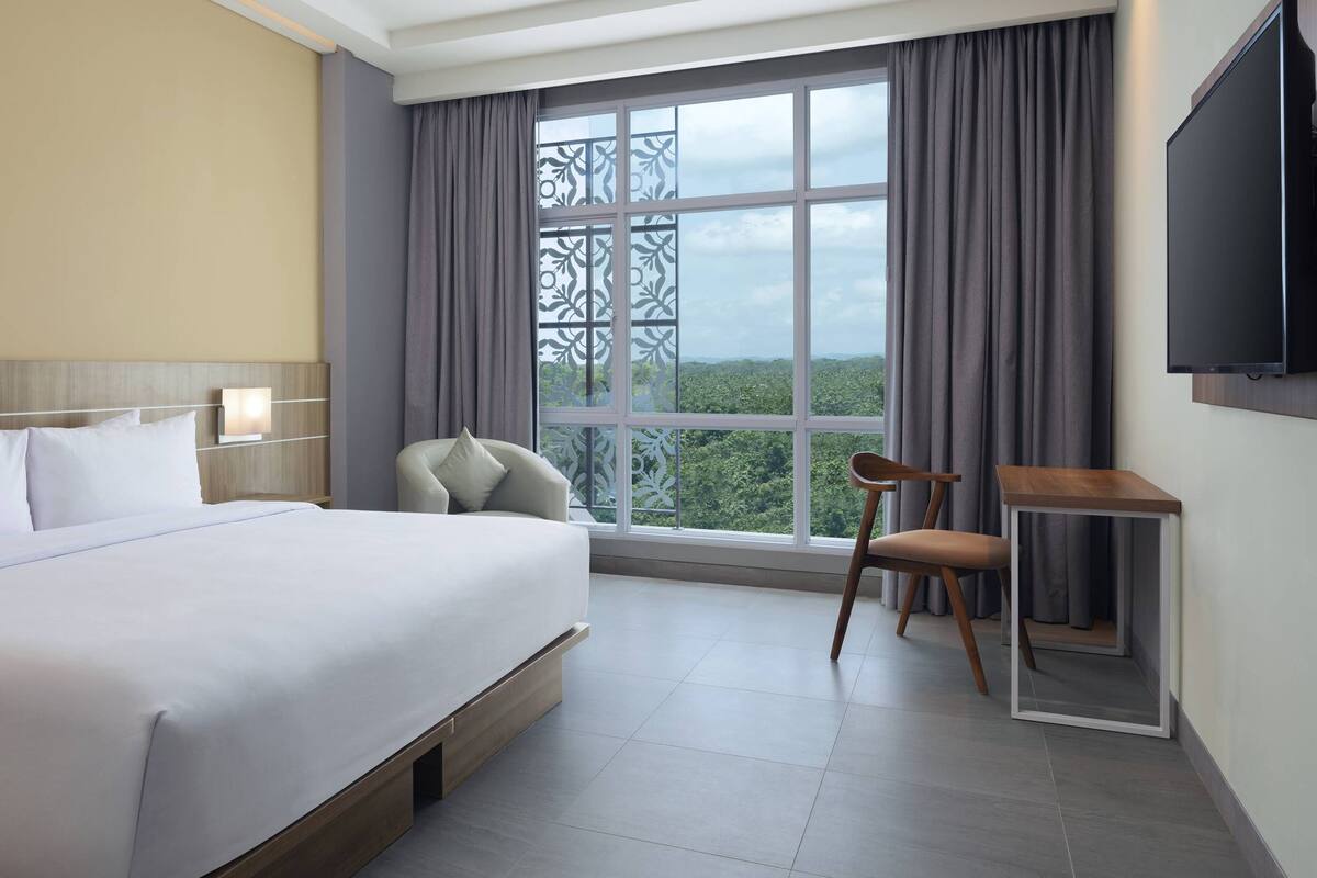 Una habitación de hotel con una cama grande, un escritorio, una silla, un televisor y una ventana con vistas.