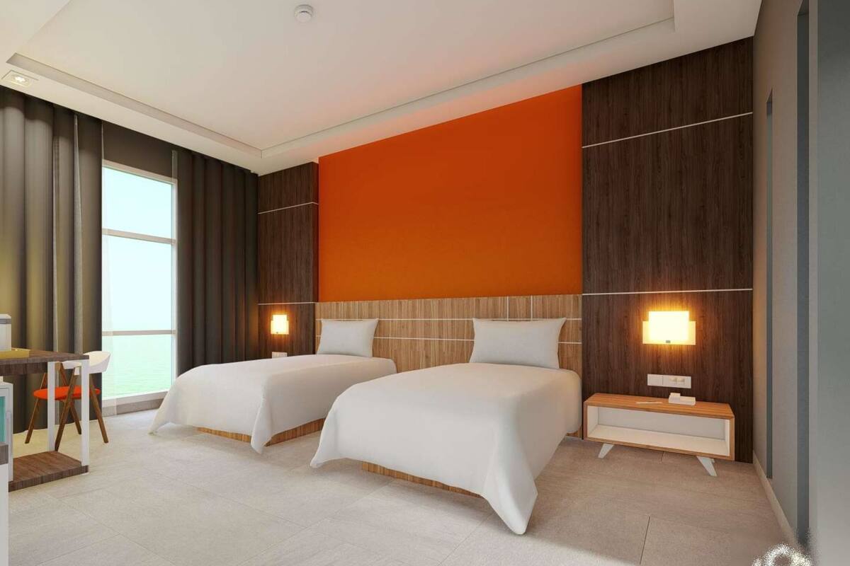 Ein Hotelzimmer mit zwei Betten, einem Schreibtisch mit Stuhl, einem kleinen Badezimmer und einem großen Fenster.