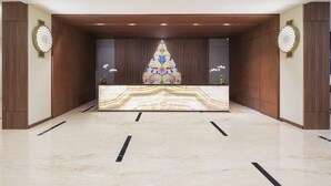 A reception area with a marble counter, wooden paneling, and decorative wall art. - Hotel Santika Gunungkidul (Playen)