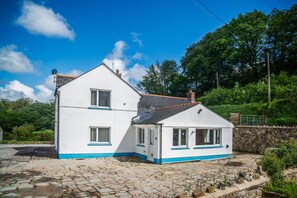 Un bâtiment blanc à deux étages, orné de bordures bleues, avec une cour pavée de pierres et un mur en pierre.