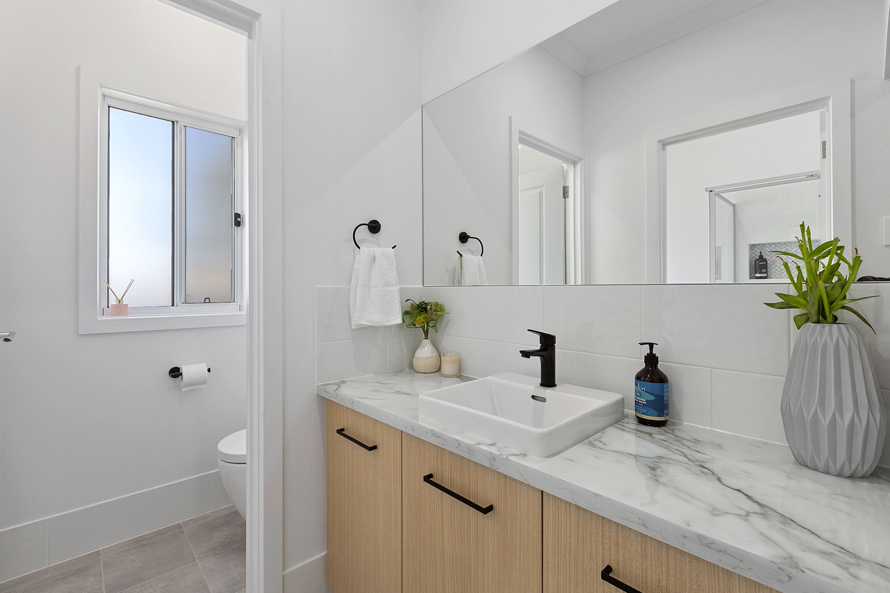 A modern bathroom with a white sink, a large mirror, and wooden cabinets.