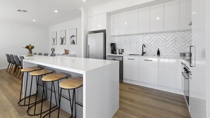 Una cucina moderna con mobili bianchi, una grande isola con sgabelli da bar, uno schienale a mosaico a spina di pesce e un frigorifero in acciaio inossidabile.