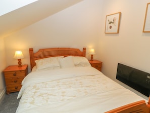 A bedroom with a wooden headboard, two bedside tables with lamps, a bed with white bedding, and a television on the wall. - Woodlands (Keighley)