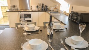 Uma cozinha moderna com eletrodomésticos embutidos, uma área de refeições preparada para quatro pessoas e vista para o exterior.
