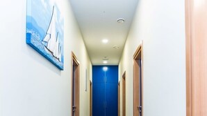 A hallway with a blue and gray patterned floor, a blue door at the end, and a painting of a sailboat on the left wall. - Ai Hostel (Split)