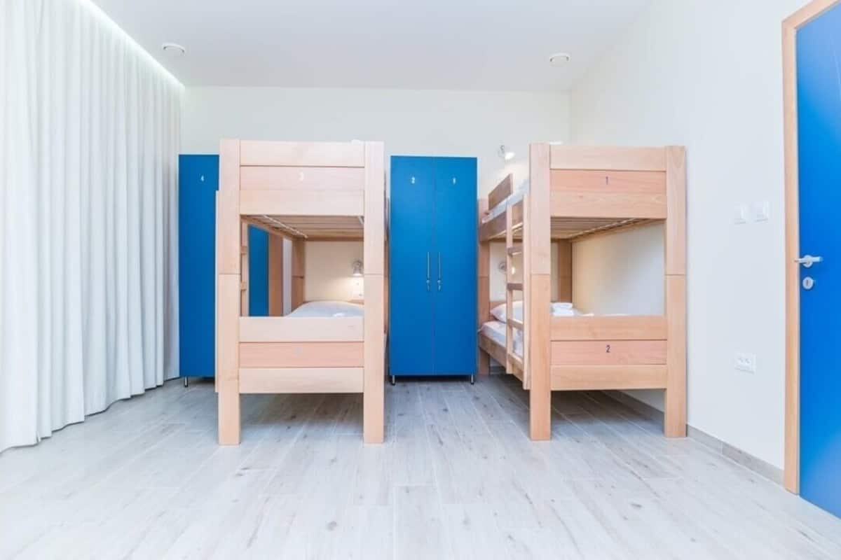 A room with bunk beds, a blue wardrobe, and a white curtain.