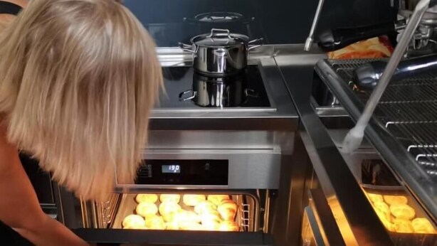 A commercial kitchen with a stainless steel oven containing baked goods. - Ai Hostel (Split)