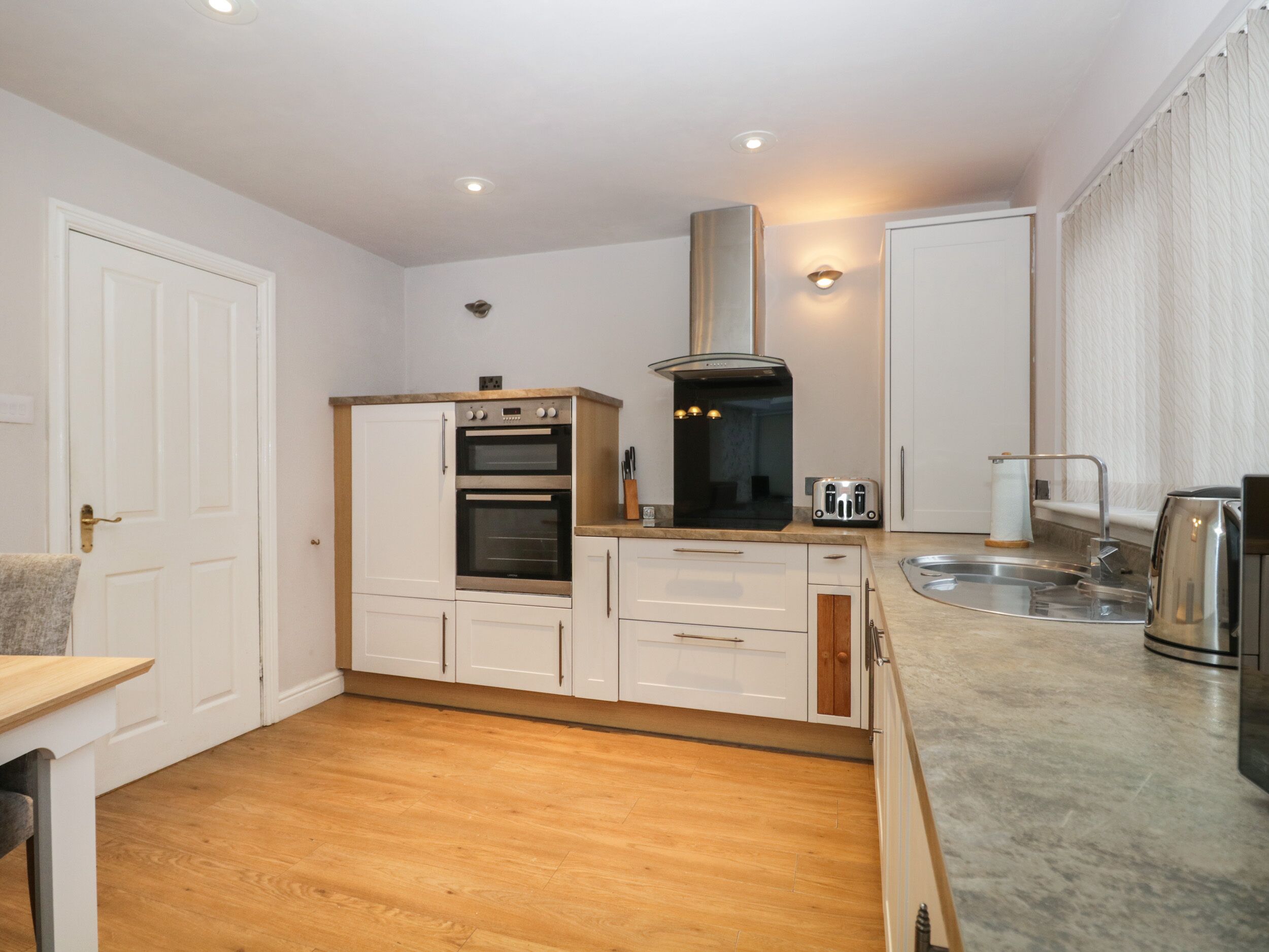 A compact kitchen with white cabinets, a built-in oven, a stainless steel range hood, a toaster, and a sink.