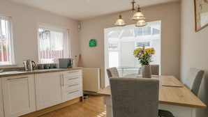 A modern kitchen with white cabinets, a wooden countertop, and a dining area with a table and chairs. - Viewpoint (Kendal)