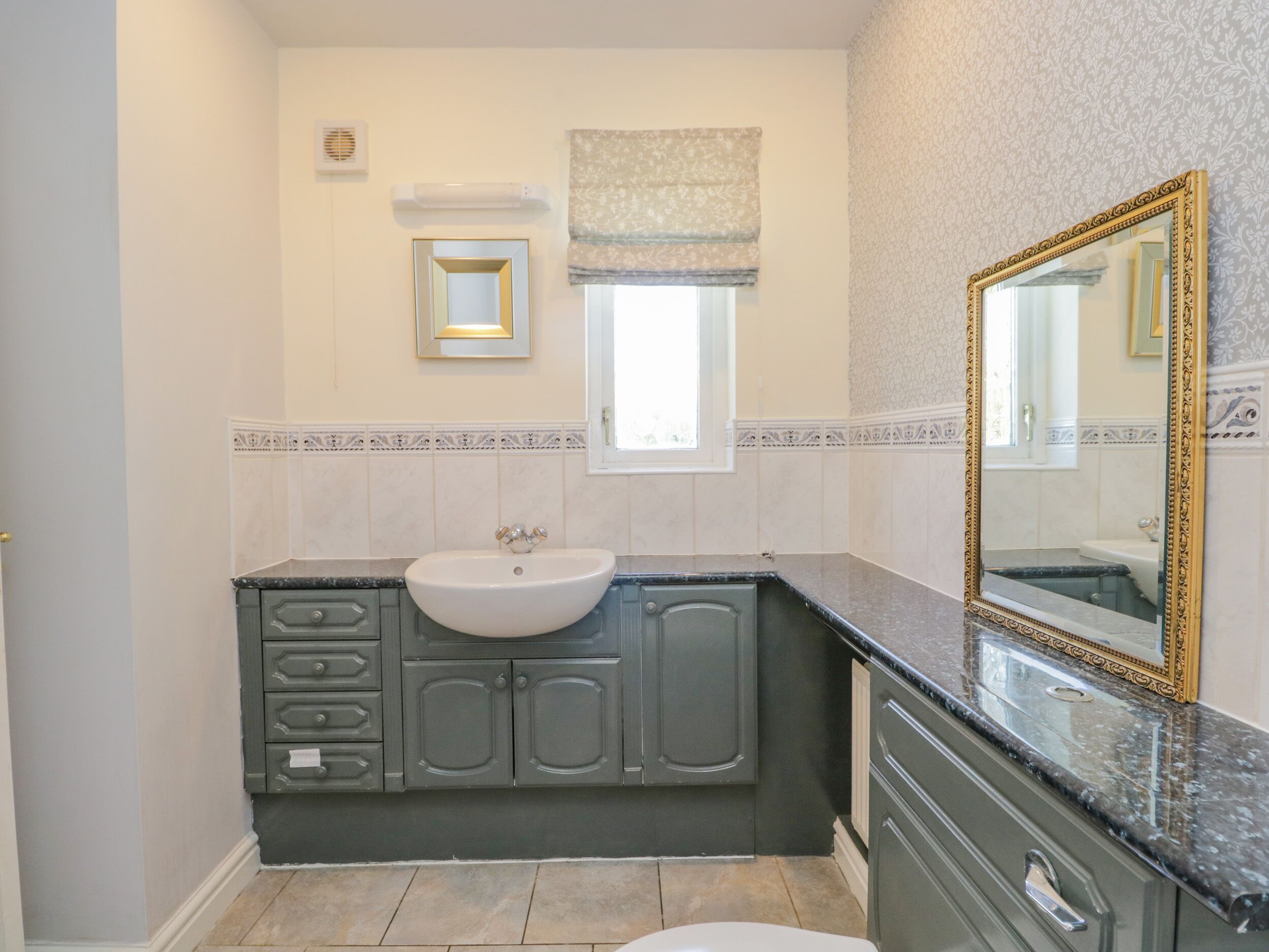 A bathroom with a white sink, dark cabinets, a large mirror, and a window with a patterned curtain.