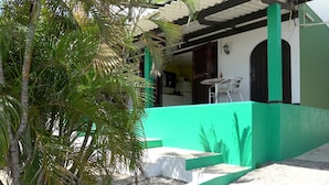 A covered outdoor area with a green wall, a small table with chairs, and a staircase leading to a door. - Apartment (Willemstad)