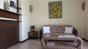 Une chambre à coucher avec un canapé à motifs, une armoire en bois, une petite table avec une lampe et un tableau abstrait aux couleurs vives accroché au mur.