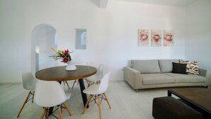 A modern living room with a round dining table, white chairs, a grey sofa, and a coffee table. There are three abstract paintings on the wall. - Coral Villa With 4 Bedrooms in Paros (Paros)