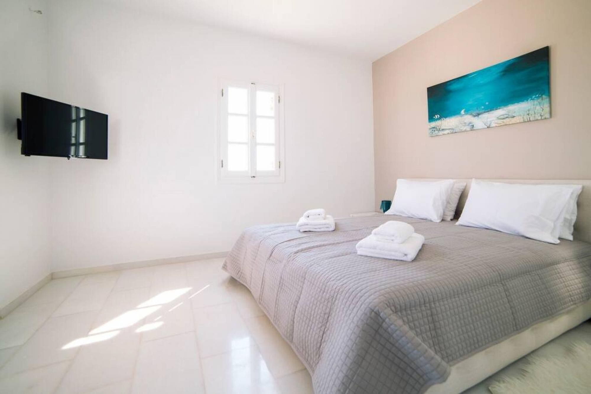 Une chambre à coucher avec un lit, un téléviseur à écran plat fixé au mur, une fenêtre et un tableau.
