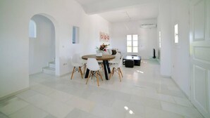 A spacious, well-lit room with a dining area featuring a round table and chairs, a sofa, and a TV. - Coral Villa With 4 Bedrooms in Paros (Paros)