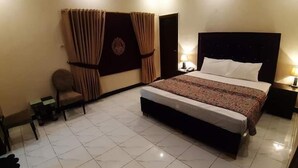 A hotel room with a large bed, a chair, a desk, and curtains. - Hotel Royal Defence (Lahore)