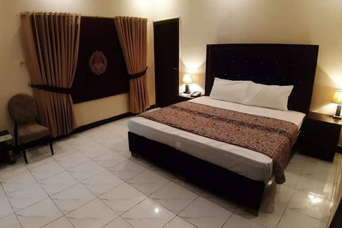 A hotel room with a large bed, a chair, a desk, and curtains.