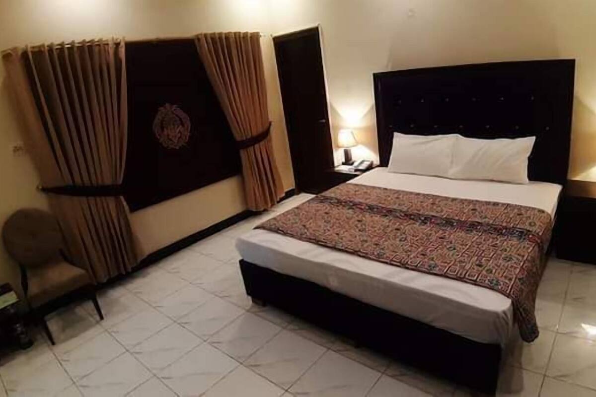 A hotel room with a large bed, two bedside tables with lamps, a chair, and curtains.