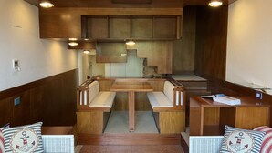 Un interior compacto y moderno con una mesa de madera central y bancos, flanqueado por sofás de mimbre con cojines de temática náutica.