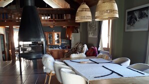 Un comedor amplio con una gran mesa de madera, sillas blancas y lámparas de mimbre colgantes.