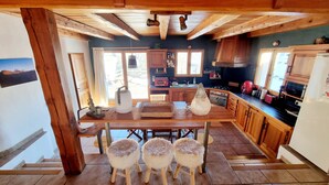 Una cocina rústica con vigas de madera, una mesa de comedor con taburetes y vistas al exterior.