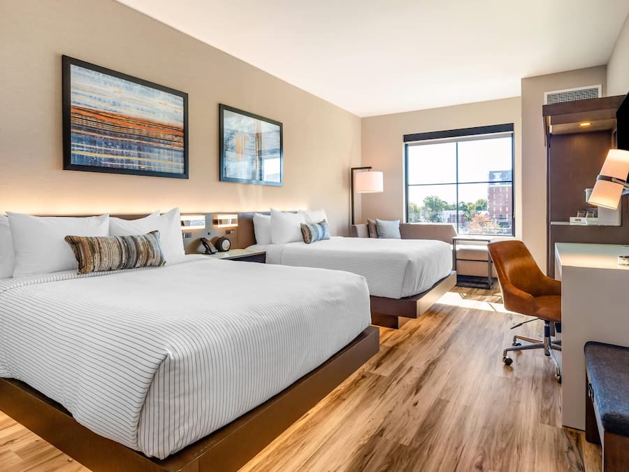 A hotel room with two beds, a desk, a chair, and a large window.