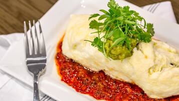 A white plate with a rolled dish topped with green garnish, accompanied by a fork on a white napkin.