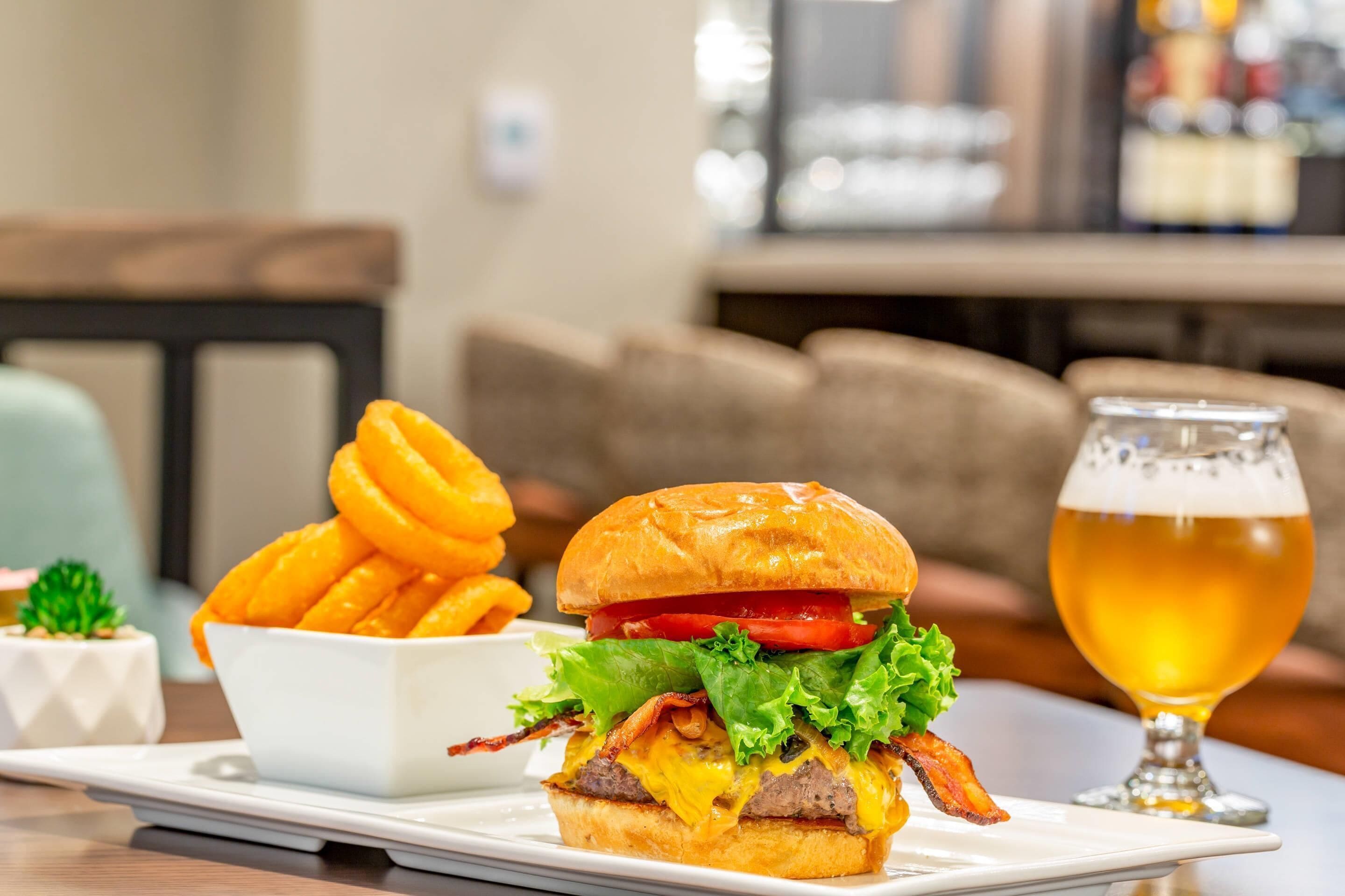 En burger med pommes frites og et glas øl på et bord.