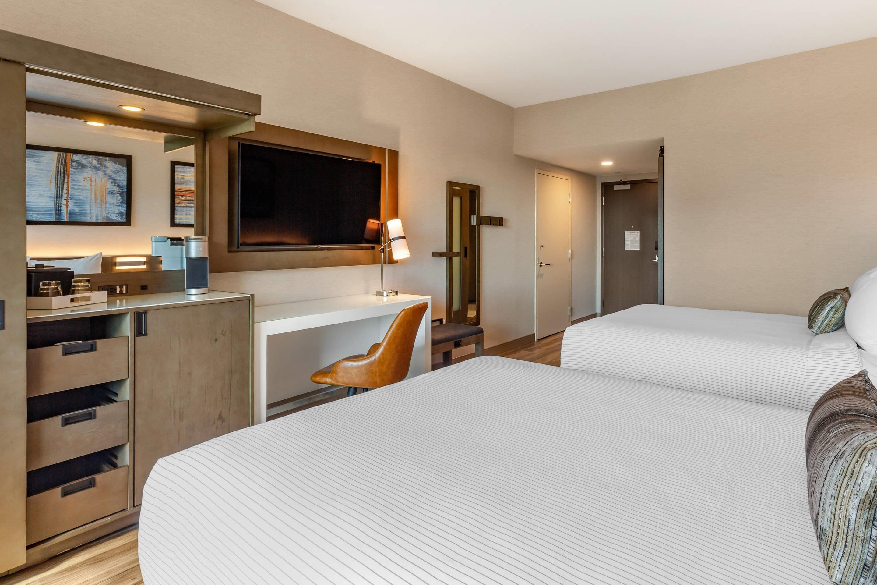 Een hotelkamer met twee bedden, een bureau, een stoel, een televisie en een kledingkast.