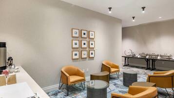 Una sala de conferencias moderna con una larga mesa, varias sillas, una máquina de café y cuadros en la pared.