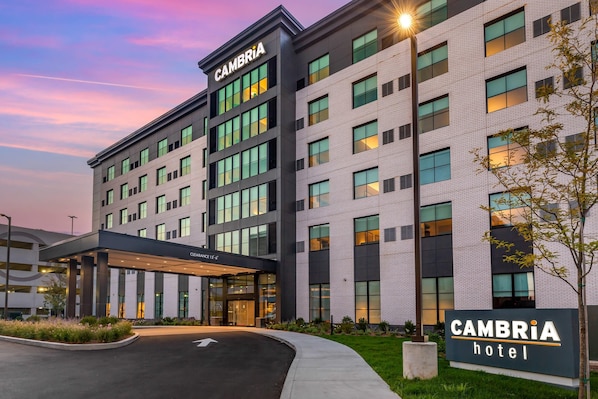 Un moderno edificio de hotel con un letrero que dice "CAMBRIA hotel" y un acceso cubierto que indica "CAMBRIA 12th".