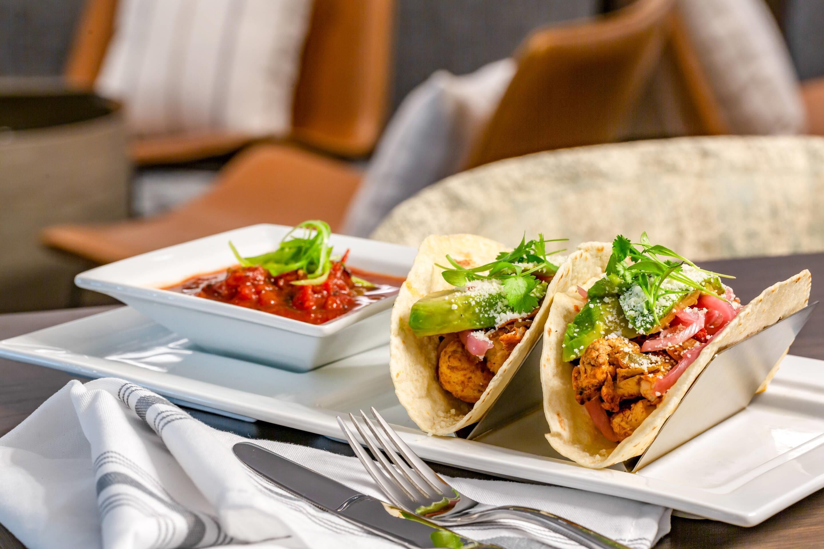Two tacos on a white plate with a side of salsa.