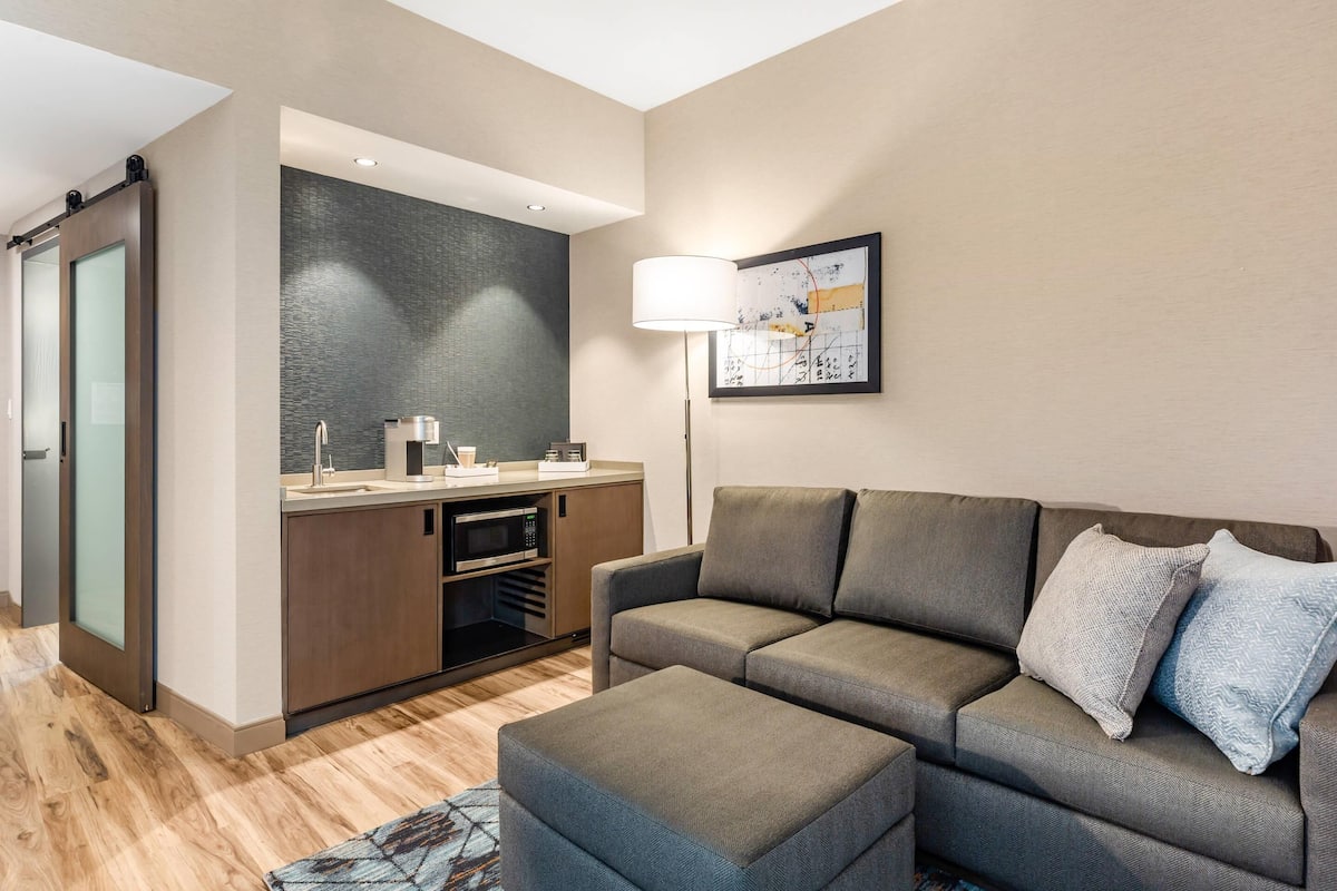 A modern living area with a sofa, ottoman, and a kitchenette.