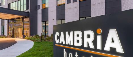 A hotel sign with the name "CAMBRIA hotel" and a modern building in the background.
