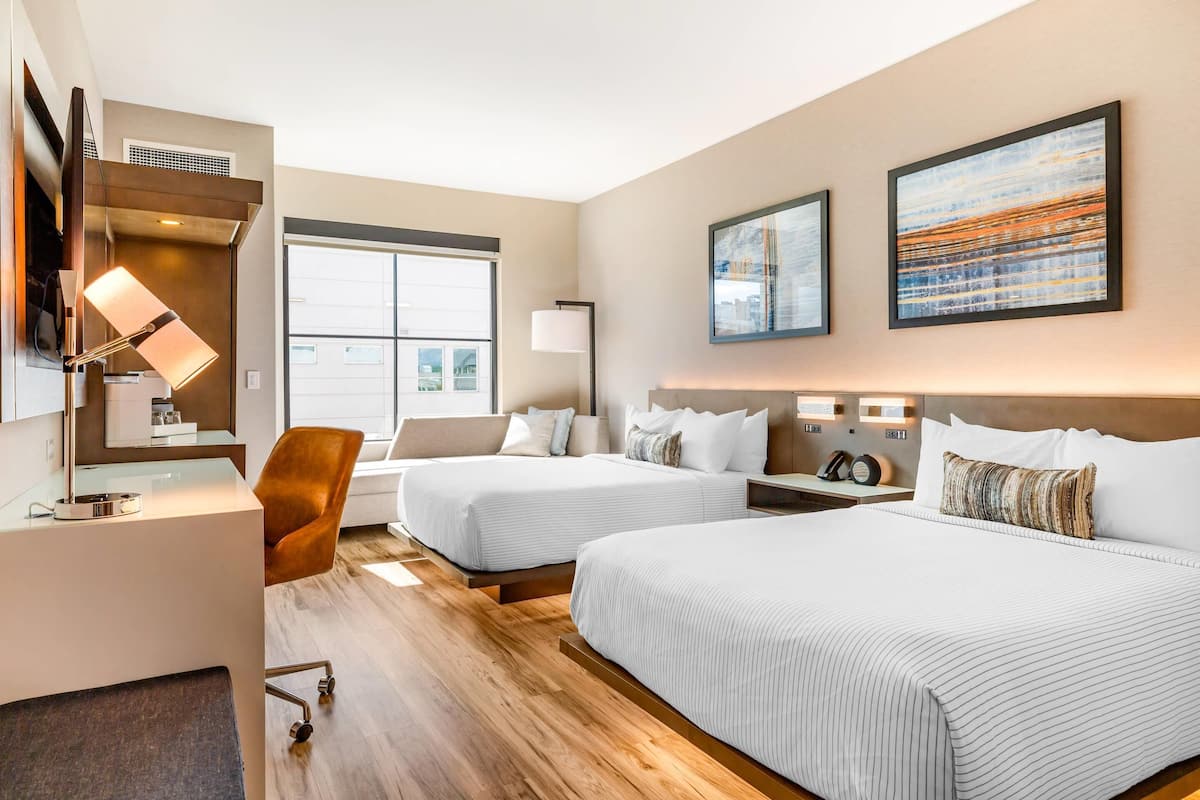 A hotel room with two beds, a desk, a chair, and artwork on the walls.