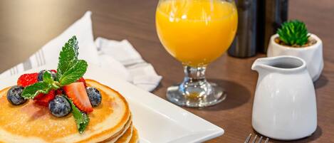 A breakfast setting with pancakes topped with strawberries and blueberries, a glass of orange juice, and a small pitcher.