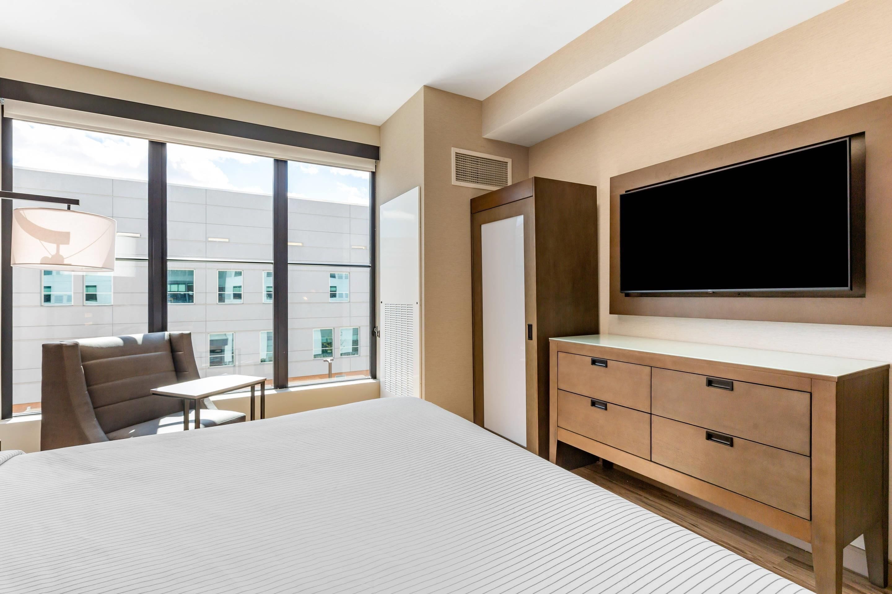 Habitación de hotel con una cama grande, un escritorio, una silla, un televisor y un armario.