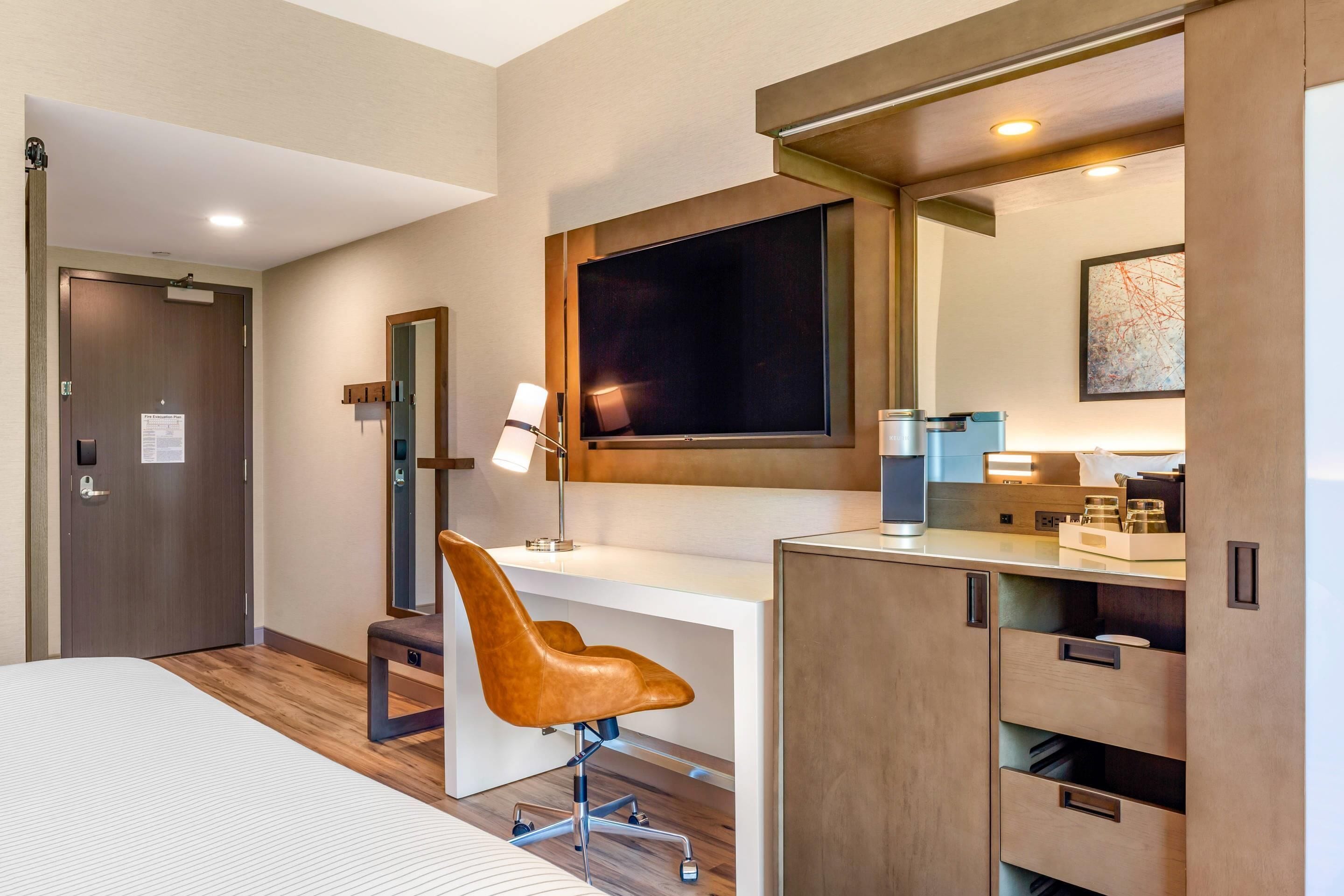 Une chambre d’hôtel moderne équipée d’un lit, d’un bureau, d’une chaise, d’une télévision et de rangements intégrés.