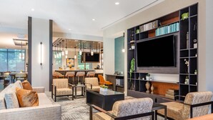 A modern living room with a large flat-screen TV, comfortable seating, and a bookshelf filled with books and decorative items. - Cambria Hotel New Haven University Area (New Haven)