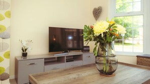 Un salon avec une table basse en bois, un téléviseur posé sur un meuble et un vase avec des fleurs sur la table.